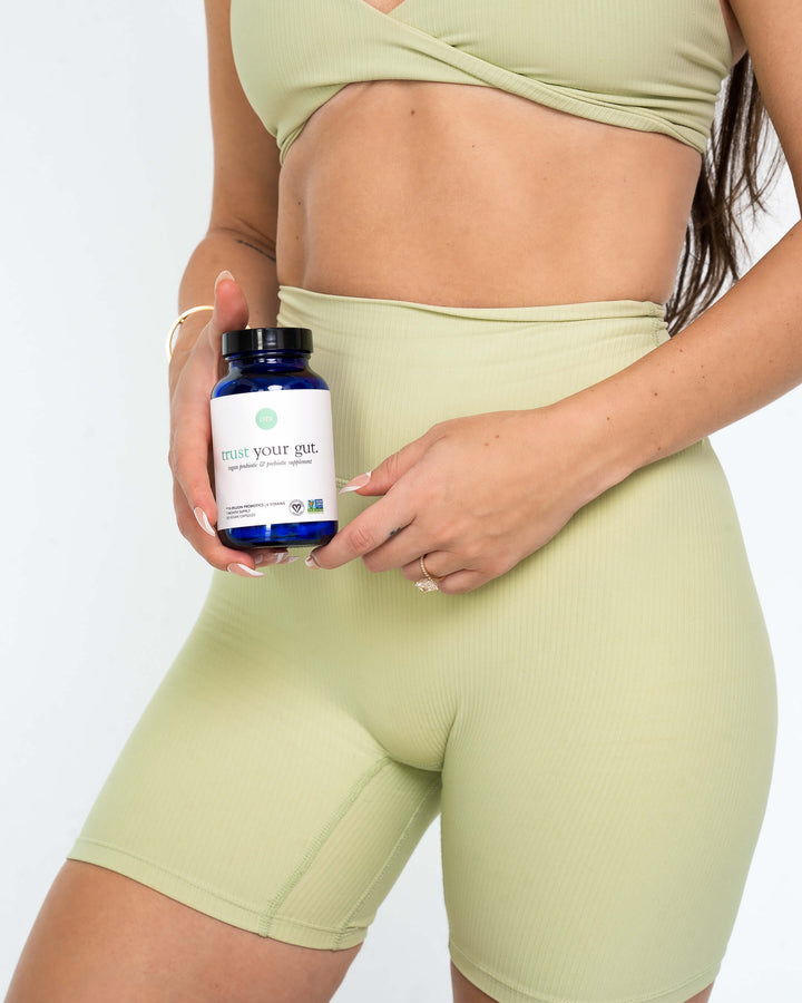 Woman in green workout gear holding trust your gut capsules by stomach