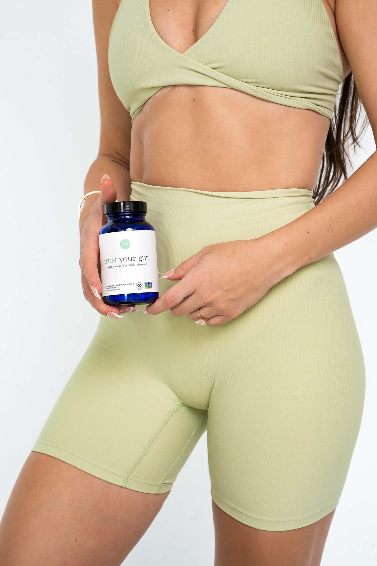 Woman in green workout gear holding trust your gut capsules by stomach