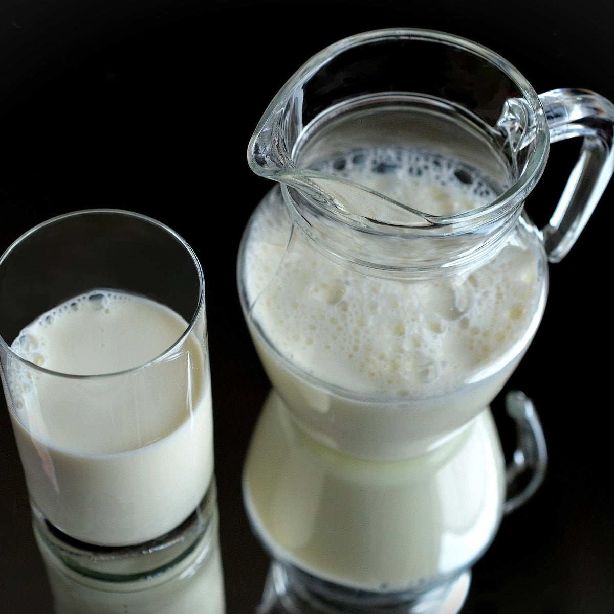 A glass and a pitcher of milk against a black background