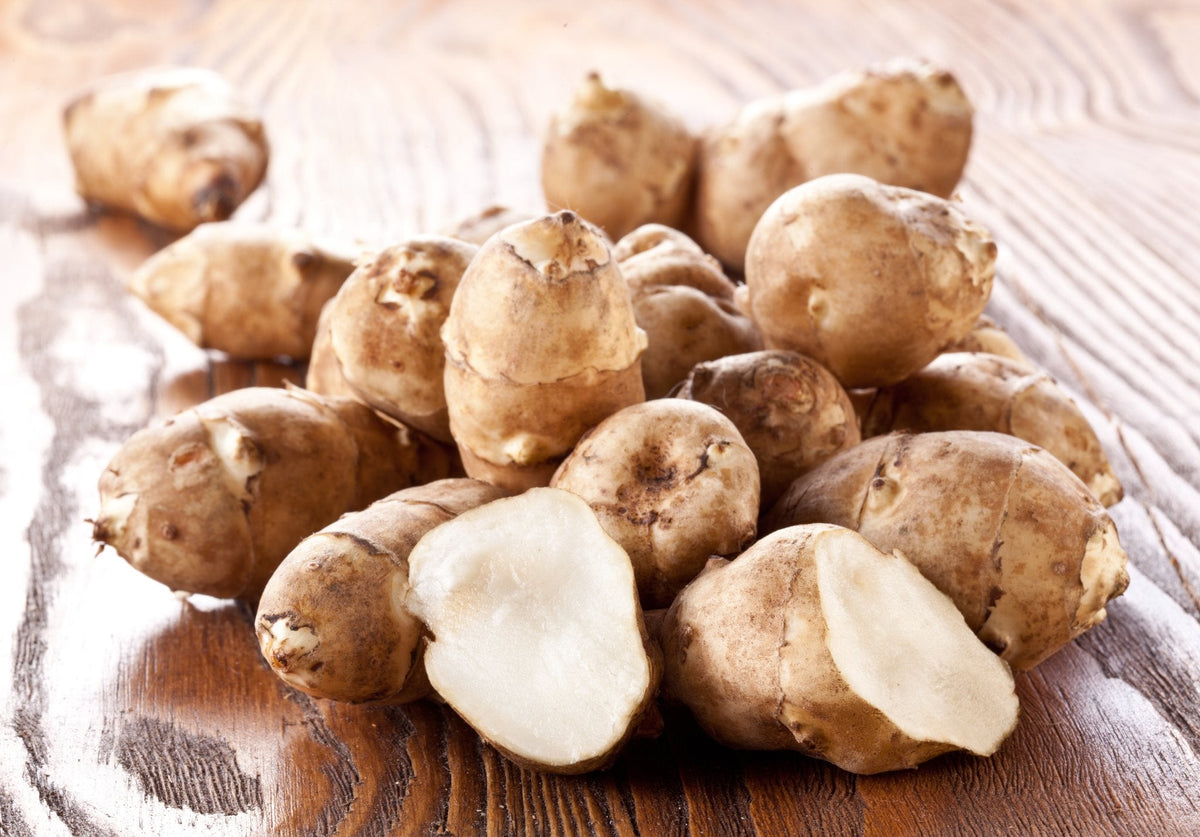 A pile of Jerusalem artichokes, one cut open, on a wooden table