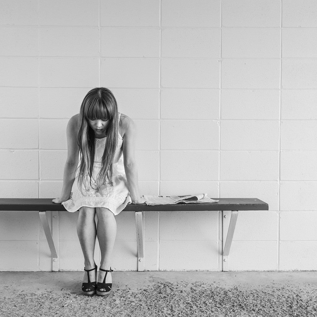 Black-and-white photo of a woman sitting on a bench with her head bowed
