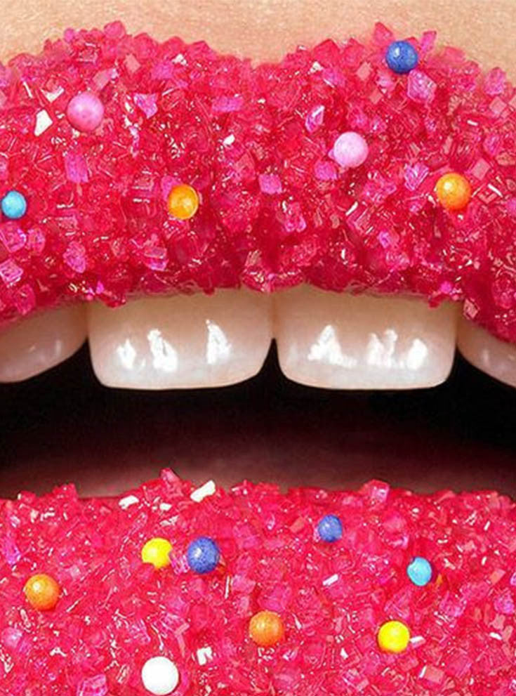 Close-up of an open mouth with lips coated in pink sugar crystals and candy sprinkles