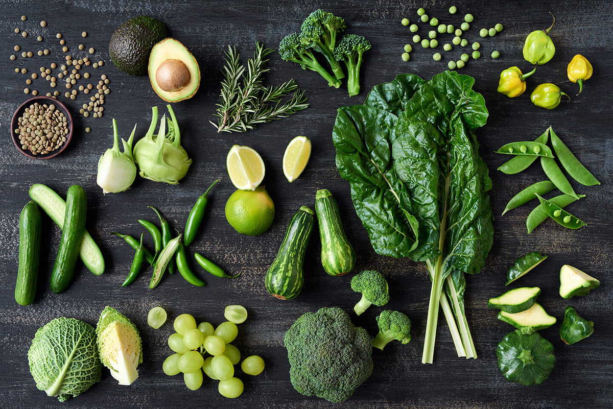 Overhead view of green vegetables, herbs and fruit on a dark surface