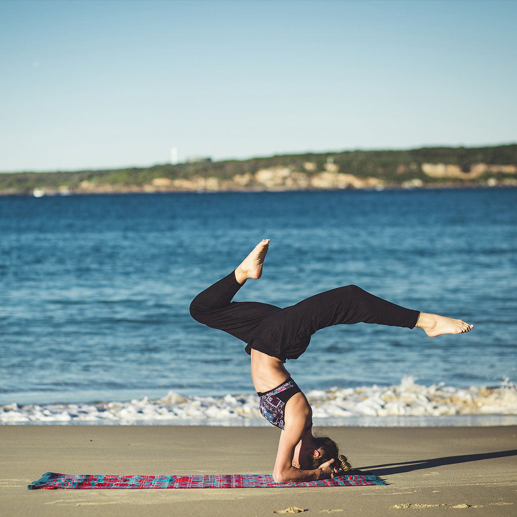 Woman in a yoga pose with her legs raised on a mat on a sandy beach by the sea