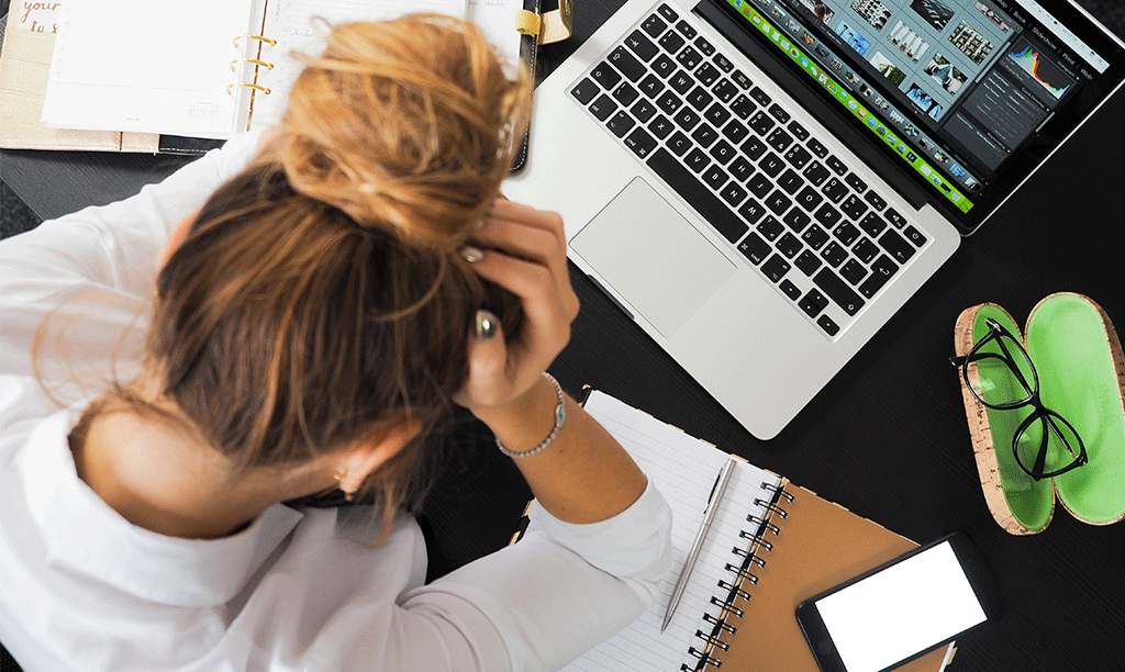 Stressed woman holding her head in her hands over a laptop and notebook