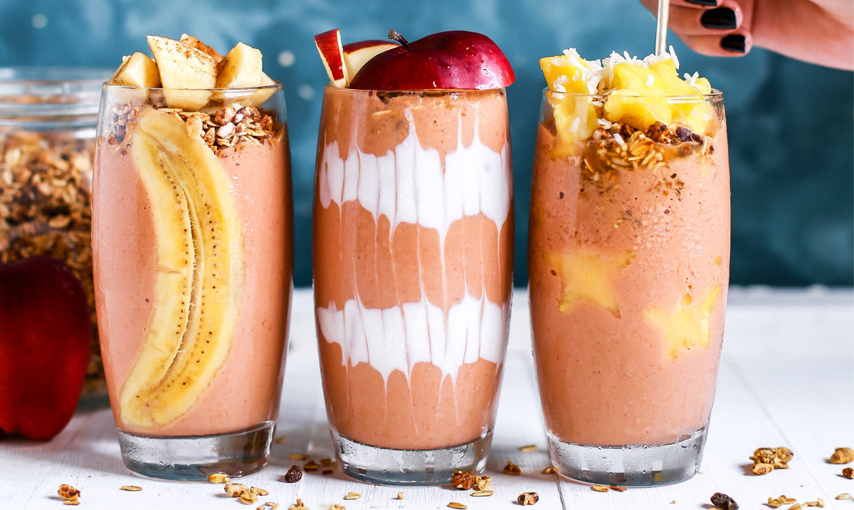 Three fruit smoothies in tall glasses topped with sliced fruit and granola