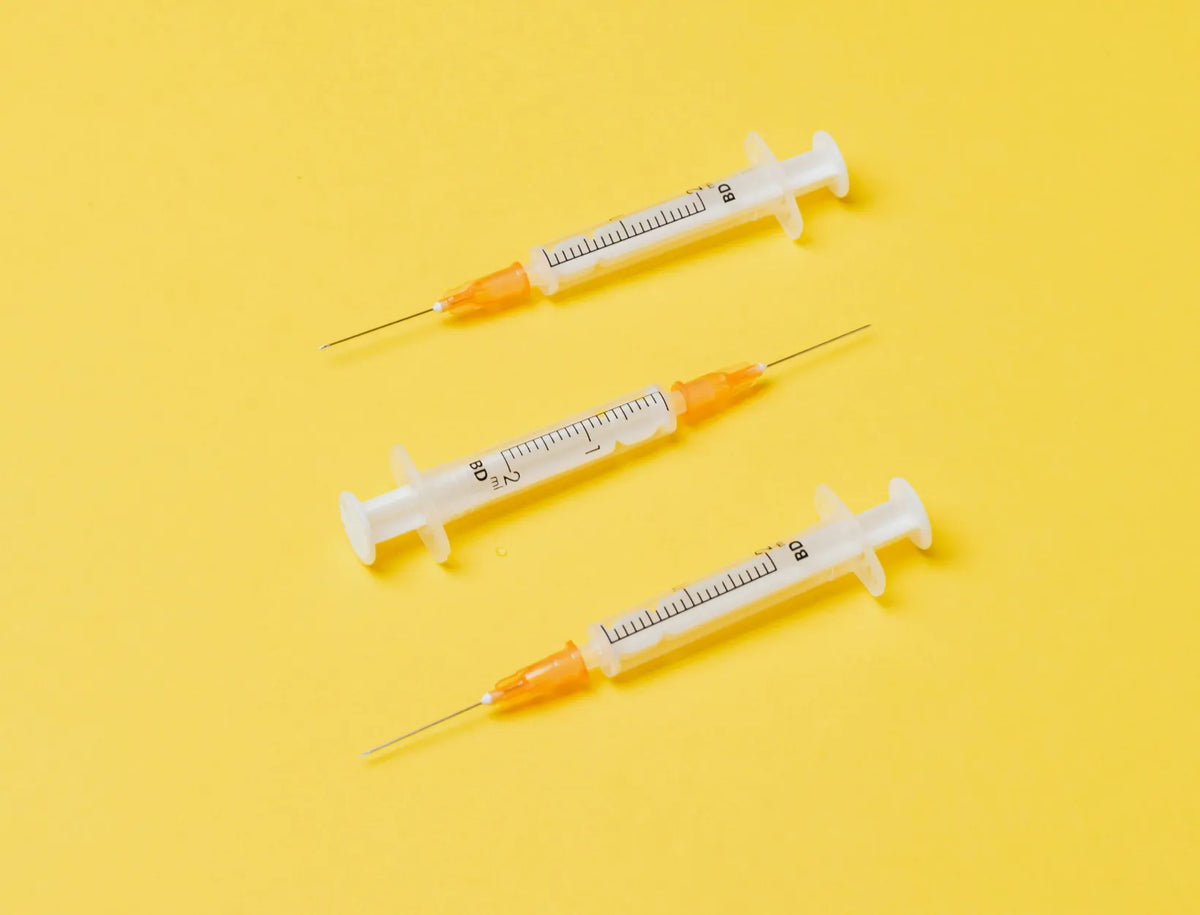 Three syringes with orange caps laid out on a yellow background
