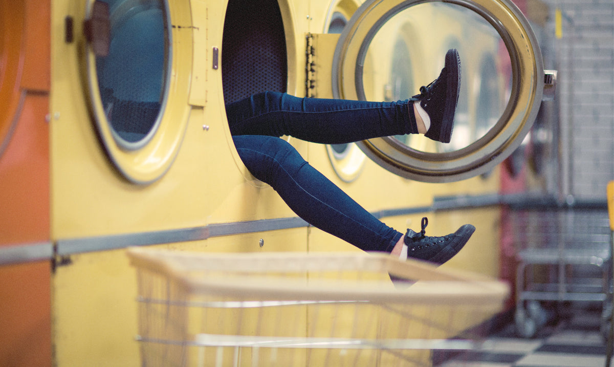 Person's legs climbing out of a front-loading washing machine at a laundromat