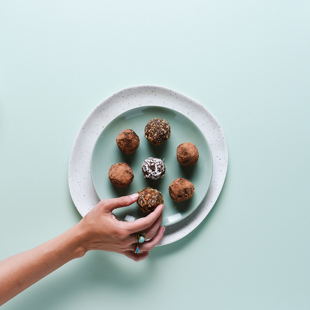 A hand reaching for assorted truffles on a plate.