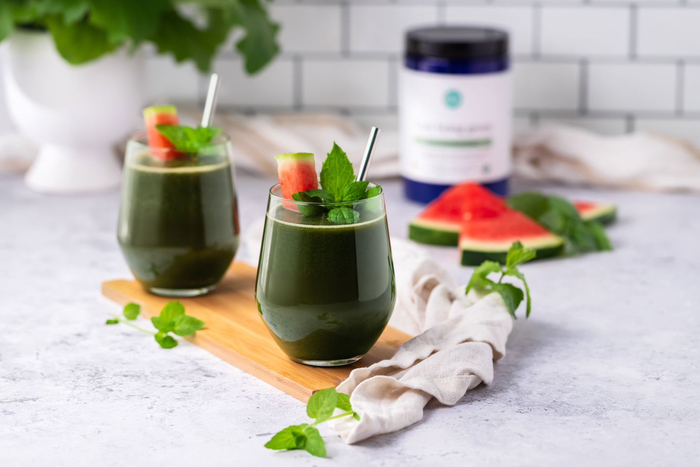 Two green smoothies with mint and watermelon garnishes on a wooden board.