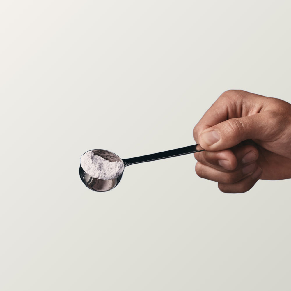 A hand holding out a scoop of creatine powder.
