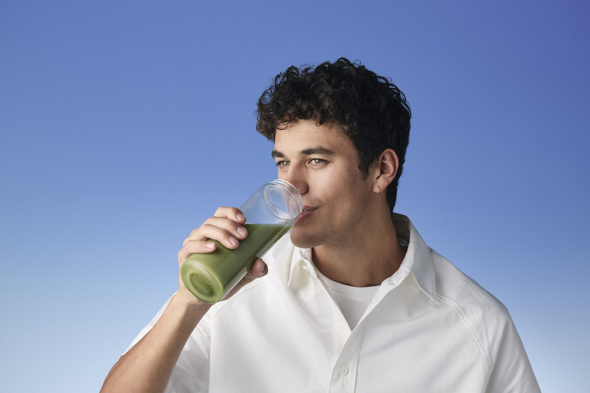 Man drinking a green smoothie from a clear glass against a blue sky
